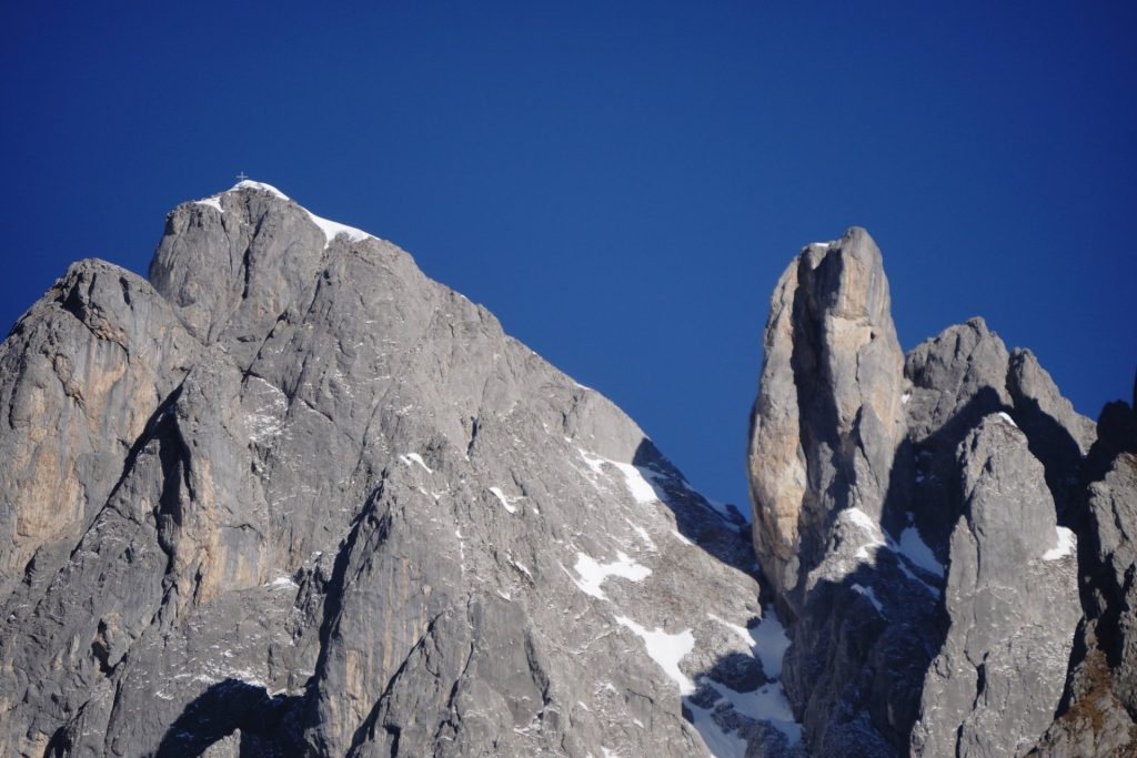 Felsige Berggipfel mit Gipfelkreuz und Schneefeldern unter blauem Himmel